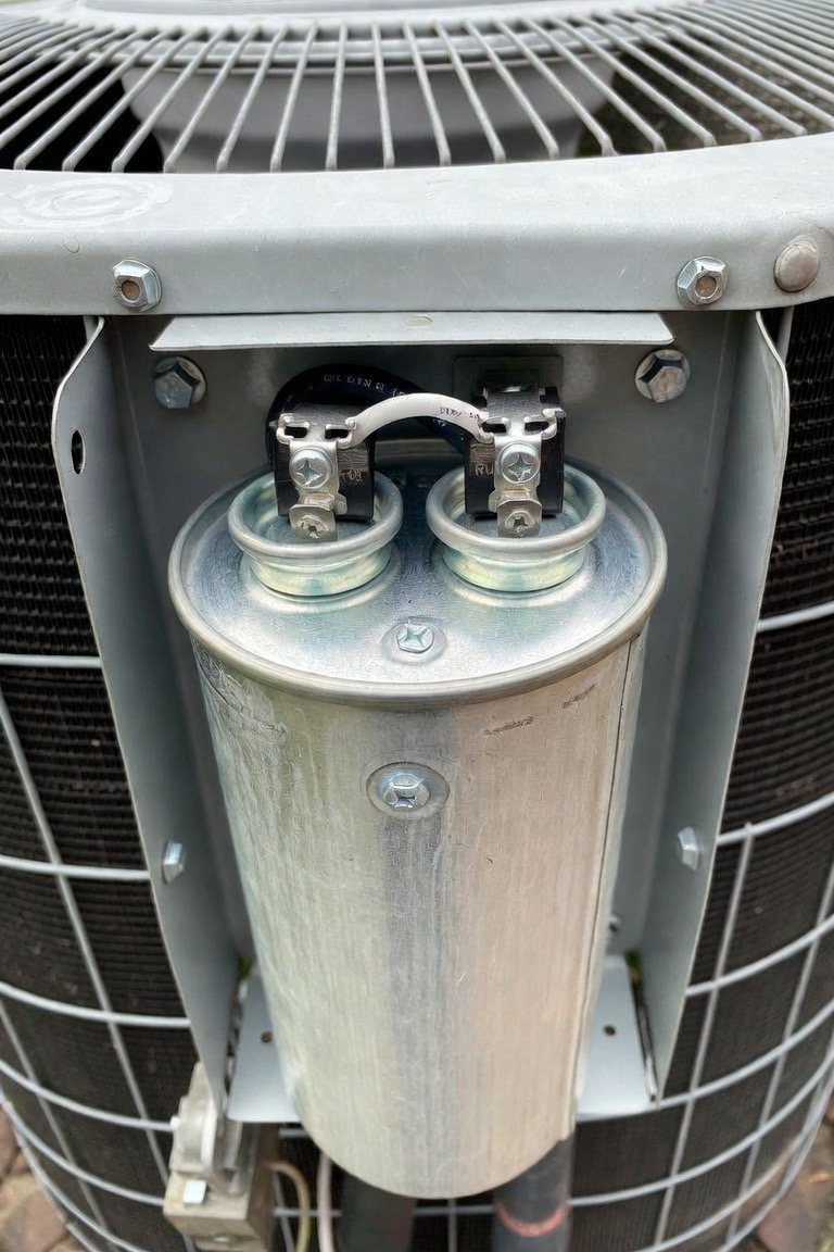 Close-up of a dual-run capacitor inside an outdoor AC condenser unit